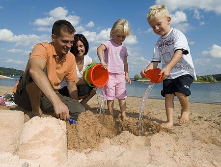 Eine Familie baut am barrierefreien Sandstrand von Ramsberg eine Sandburg