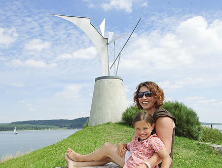 Mutter und Tochter sitzen auf der Wiese zu Füßen der Phoenix-Statue bei Ramsberg am Brombachsee