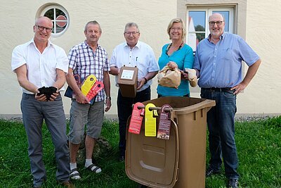 Biotonne Infokampagne Gruppenbild von mehreren Menschen, die hinter einer geöffneten Biotonne stehen, an der Infokarten hängen