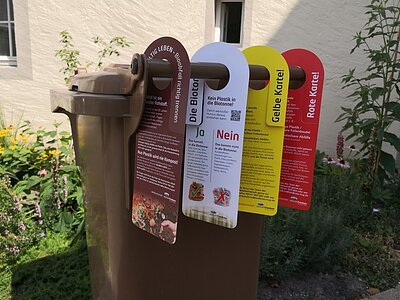 Kommunale Abfallwirtschaft Biotonne mit vier Tonnenanhängern für richtig sortierte Bioabfälle zur Kompostierung, kein Plastik in die Biotonne, Verwarnung falsch befüllte Tonne Gelbe Karte, falsch befüllte Tonne Rote Karte - der Müll wird nicht geleert.