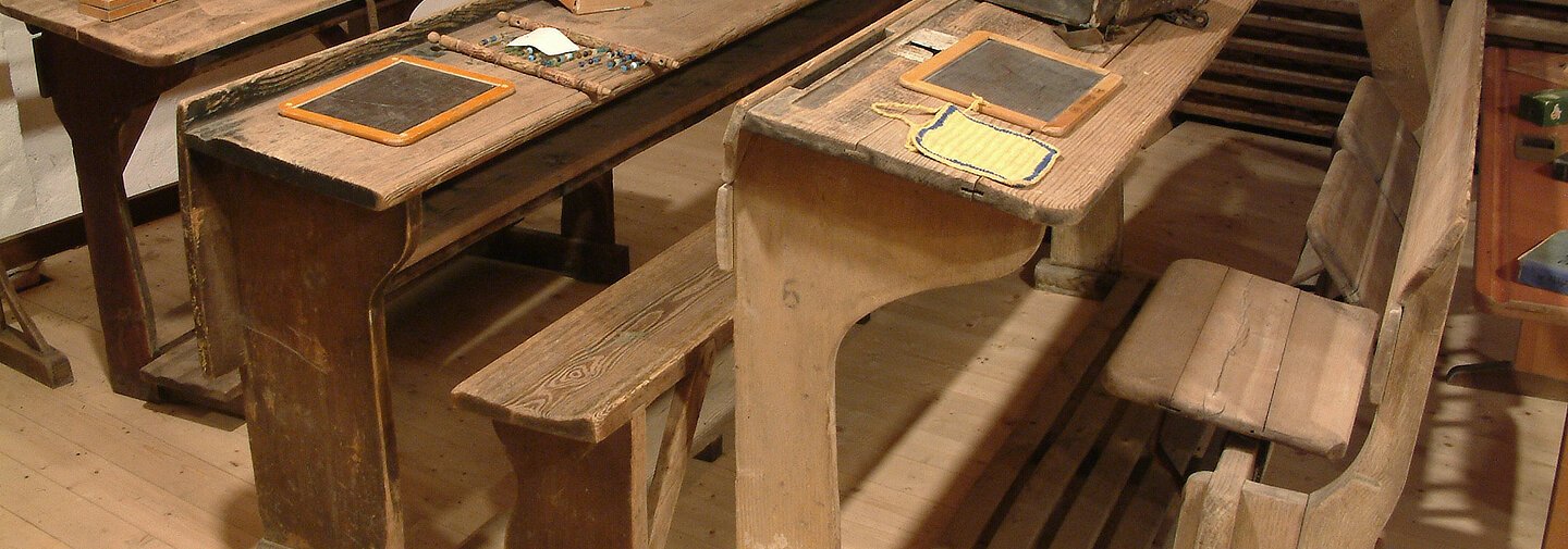 Auf alten Schulbänke liegen alte Taschen und Tafeln.