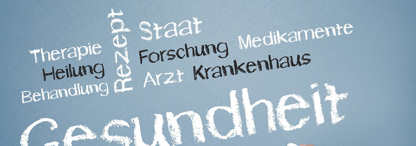 Wortwolke mit Kreide geschrieben. Der Text Gesundheit steht in weiß im Vordergrund.
