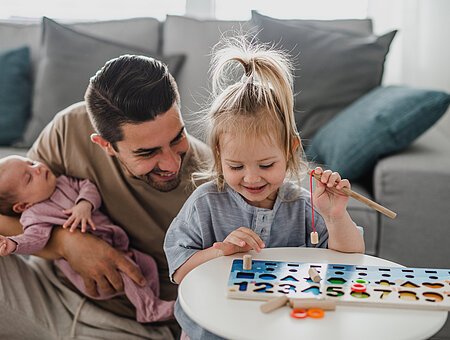 A happy young man taking care of his newborn baby and little daughter indoors at home, paternity leave.