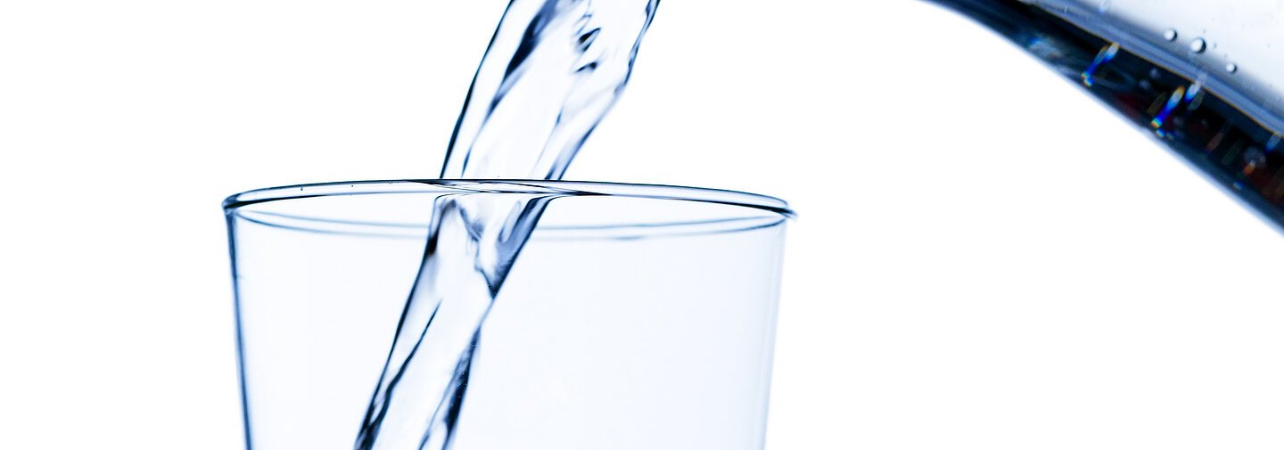 Reines und sauberes Wasser wird von einer Wasserkaraffe in ein Glas eingeschenkt.