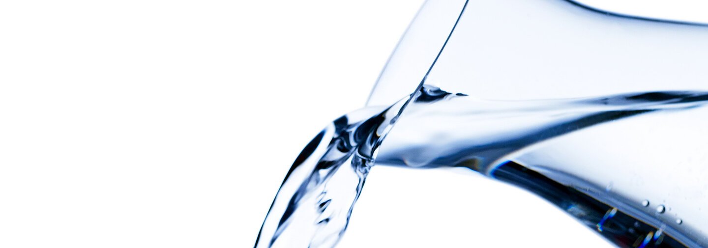 Reines und sauberes Wasser wird von einer Wasserkaraffe in ein Glas eingeschenkt.